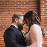 A candid bride and groom embrace in front of a brick wall at Savage Mill on their wedding day.