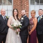 The wedding party, including the bride and groom, poses for portraits in front of The Great Room at Savage Mill.