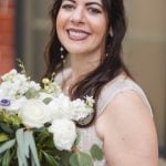 A bride holding a bouquet in front of the Savage Mill, a brick building.