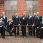 A group of groomsmen posing in front of a brick building for a wedding portrait at Savage Mill.