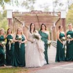 Bridesmaids in emerald dresses standing on a bridge at Savage Mill, posing for wedding portraits.