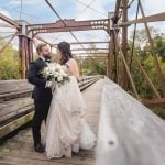 A wedding portrait of a bride and groom standing on the Savage Mill bridge in the fall.