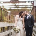 A wedding portrait of a bride and groom standing on a wooden bridge at Savage Mill.