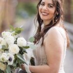 A wedding portrait of a bride smiling while holding her bouquet on a bridge at Savage Mill.