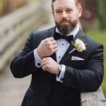 A groom in a tuxedo posing on a bridge at Savage Mill for his wedding portrait.