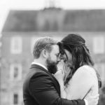 A wedding portrait of a bride and groom embracing in front of the historic Savage Mill building.