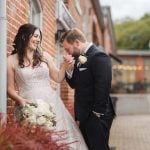 A wedding couple sharing a loving kiss in front of the rustic brick walls of Savage Mill.