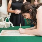 A candid bride signing her wedding vows on a green table at Savage Mill.