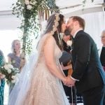 A bride and groom share a passionate kiss under a tent during their wedding ceremony at Savage Mill.