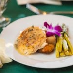 A white plate with food and a glass of wine at a wedding.