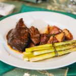 A plate with steak, asparagus and potatoes on it at a wedding celebration.