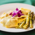 A white plate with asparagus and ravioli on it at a wedding.