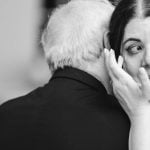 A black and white photo of a woman hugging an older man at a wedding reception.