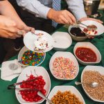 At a table in Savage Mill, a group of people enjoys bowls of candy and ice cream, savoring every delightful detail.