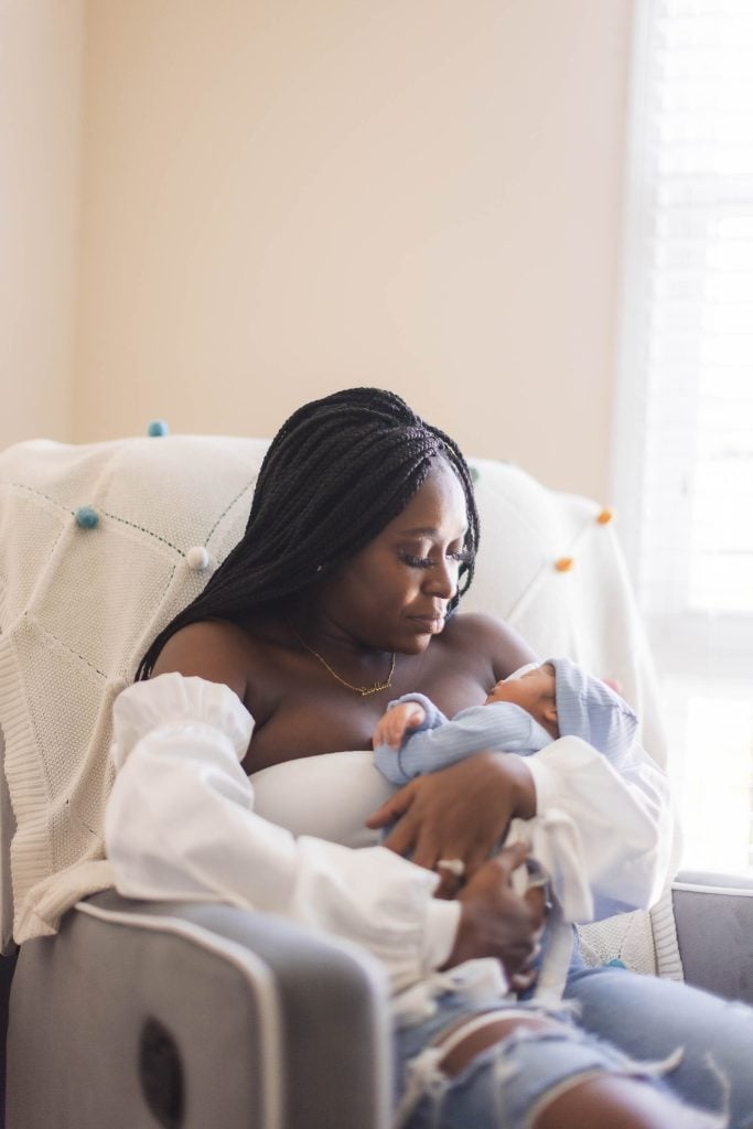 A woman is holding her newborn baby while sitting in a chair at their family home.