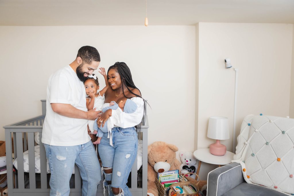 Portraits of a family in their family home, standing in front of a baby's crib.