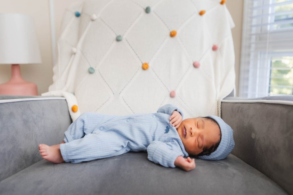 A newborn baby boy is peacefully laying on a chair in his family home, dressed in a charming blue outfit.