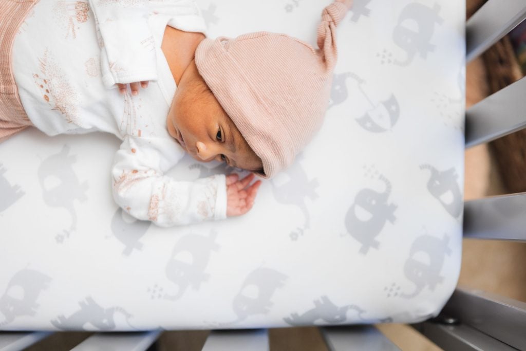 A newborn sleeping peacefully in a crib adorned with an adorable elephant print.