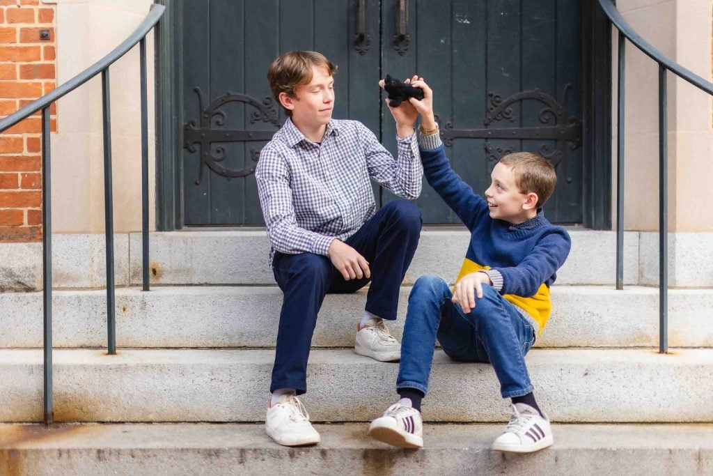 Two boys sitting on the steps of a building in Downtown Annapolis holding a camera.