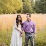 An engaged couple holding hands in a field of tall grass at Patuxent Research Refuge during sunset in Maryland.