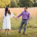 An engaged couple holding hands in a field at Patuxent Research Refuge, capturing their beautiful connection as the sun sets for their engagement photos.