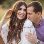 A couple is embracing on a bench in Maryland's Patuxent Research Refuge, capturing beautiful engagement photos amidst the scenic field.