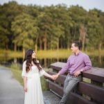 An engaged couple holding hands on a wooden bench near Patuxent Research Refuge in Maryland.