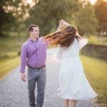 A couple is walking down a path at the Patuxent Research Refuge in Maryland with their hair blowing in the wind during sunset.