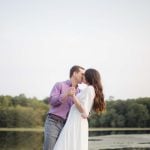 An engaged couple sharing a romantic kiss during a stunning sunset in Maryland, capturing the essence of their engagement photos at a picturesque lake.