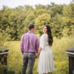 An engaged couple standing on a bridge at Patuxent Research Refuge in Maryland, admiring the beautiful sunset over the woods.