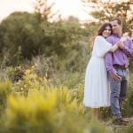 A couple embraces in the tall grass at Patuxent Research Refuge during their engagement session at sunset.