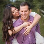 A man and woman embracing in the Patuxent Research Refuge field, capturing their love during a breathtaking sunset for their engagement photos.