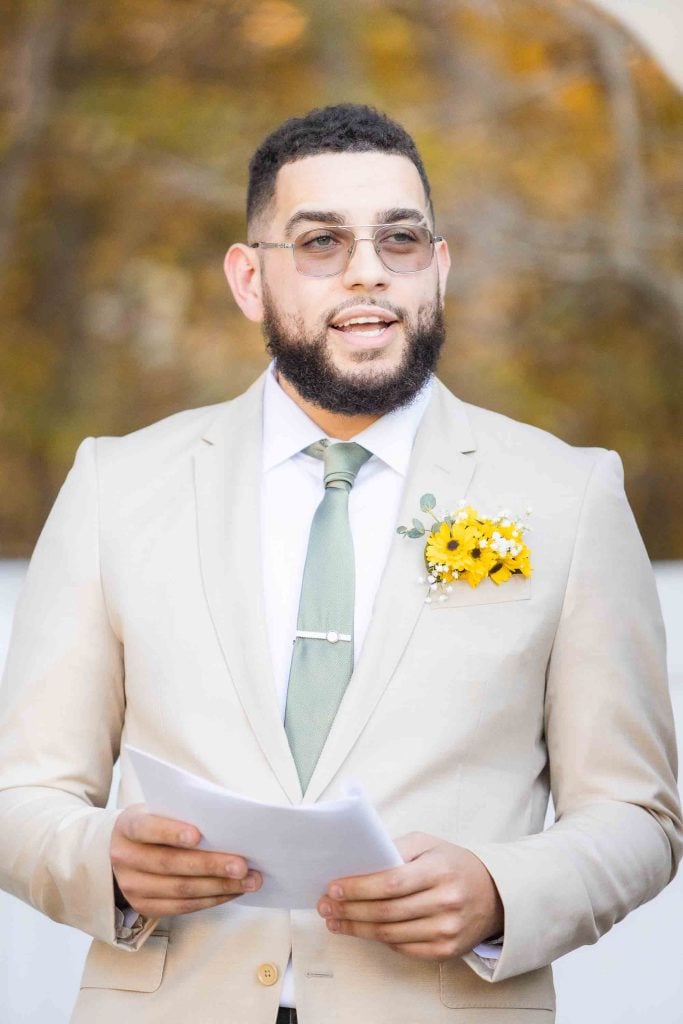 A man in a tan suit is holding a wedding invitation card.