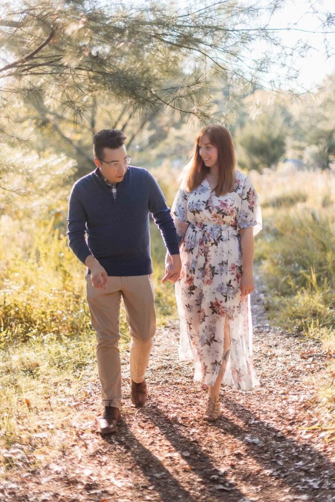 An engaged couple taking portraits in the Patuxent Research Refuge, walking down a path in the woods.