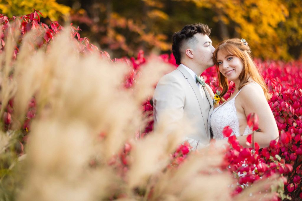 A Wedding couple is posing in a field of red flowers at Blackwall Barn & Lodge.