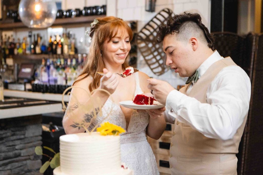 At their wedding reception, the bride and groom joyfully feed each other slices of their beautifully decorated wedding cake at the Blackwall Barn & Lodge.