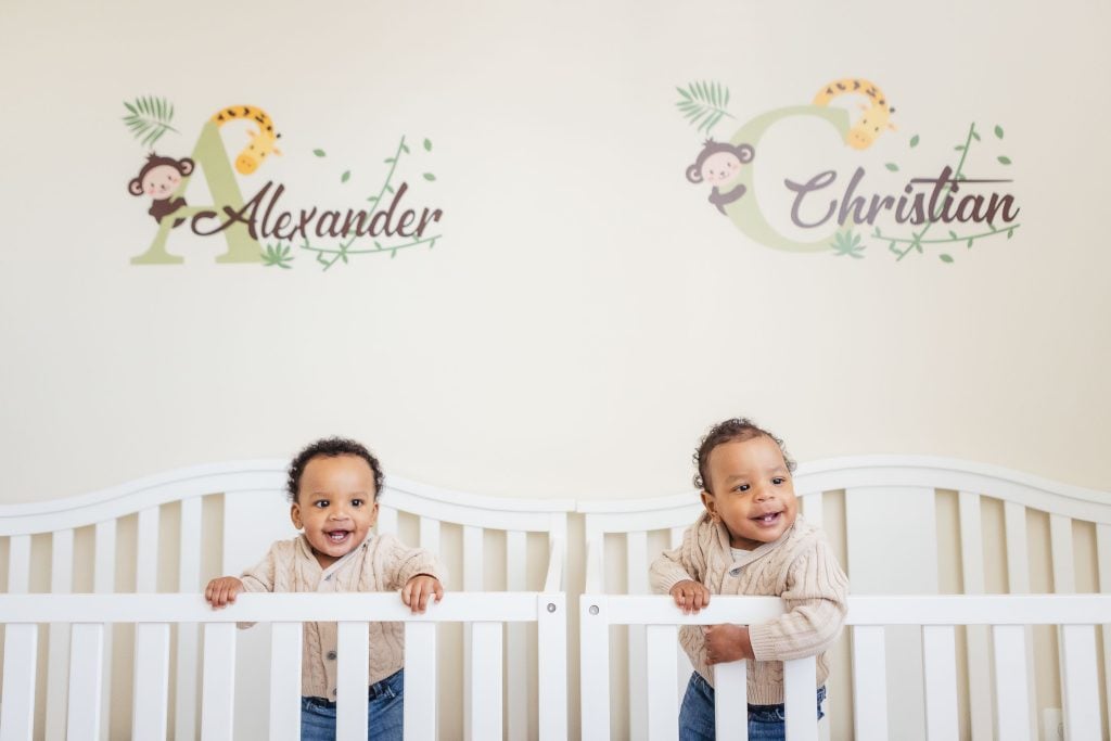 Two baby boys at home, peacefully resting in a crib, captured in heartwarming family portraits with their names proudly displayed on the wall.