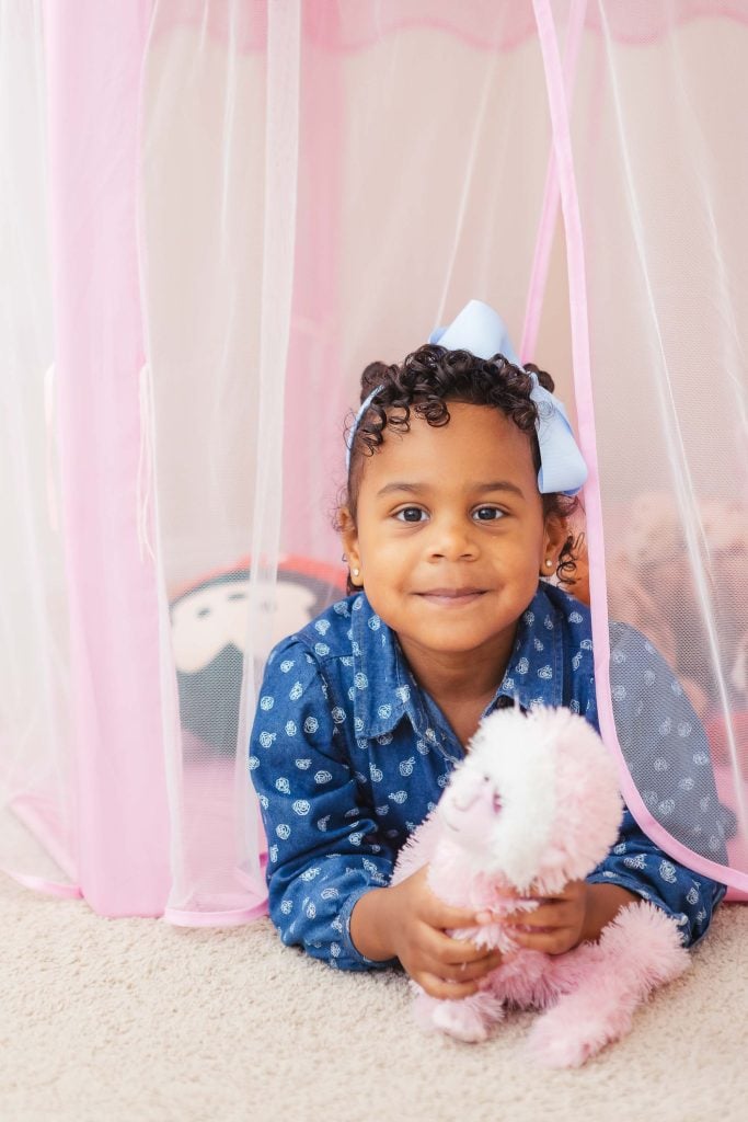 A young girl, surrounded by her stuffed animal in a cozy pink tent at home.