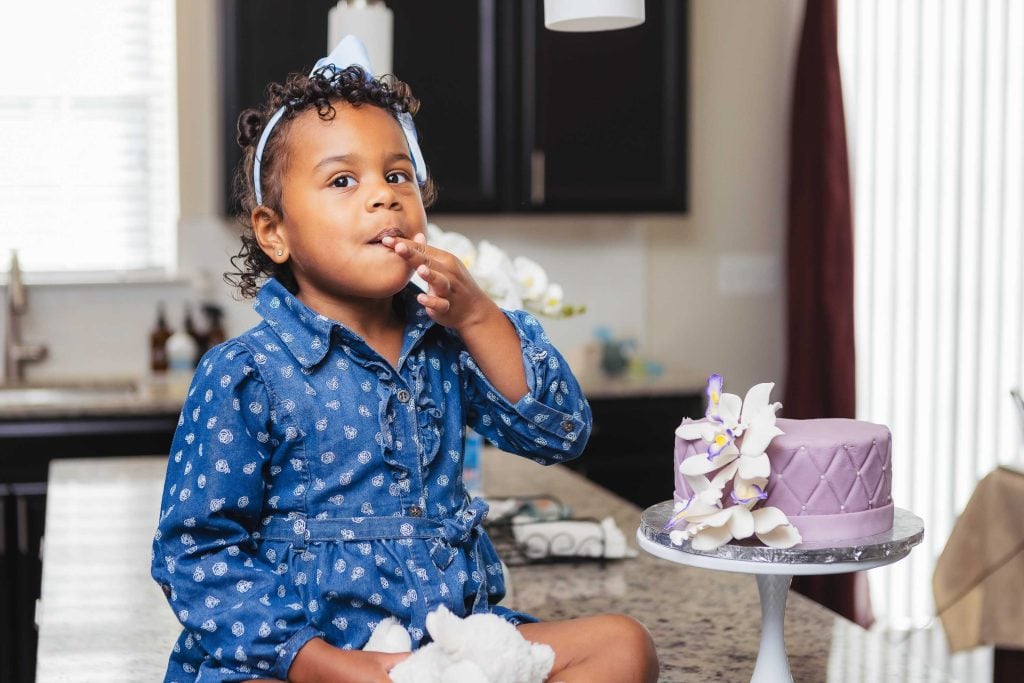 A little girl is enjoying a cake with her family at home.