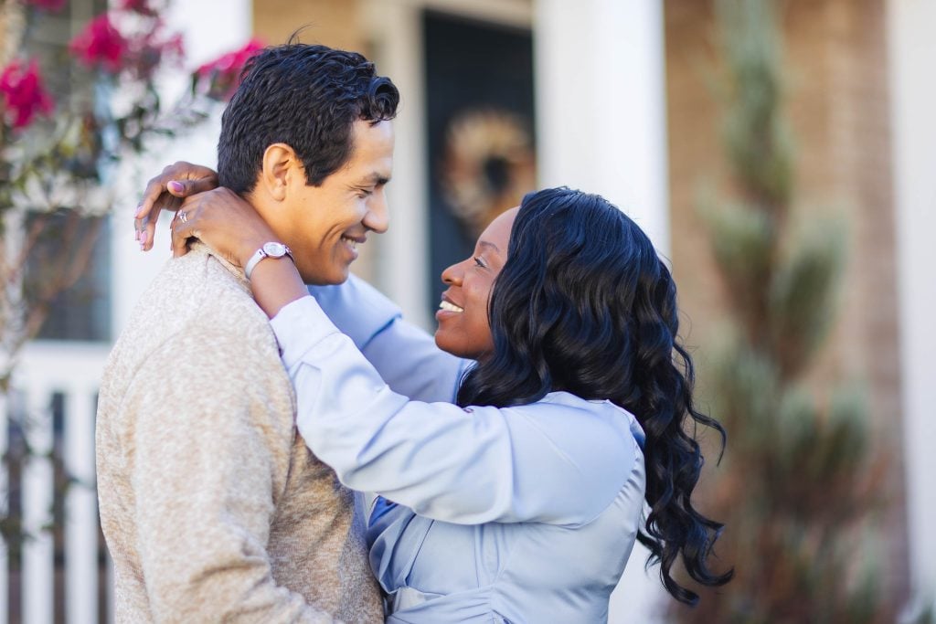 A black man and woman embracing in front of their home, capturing a heartfelt moment of family love.