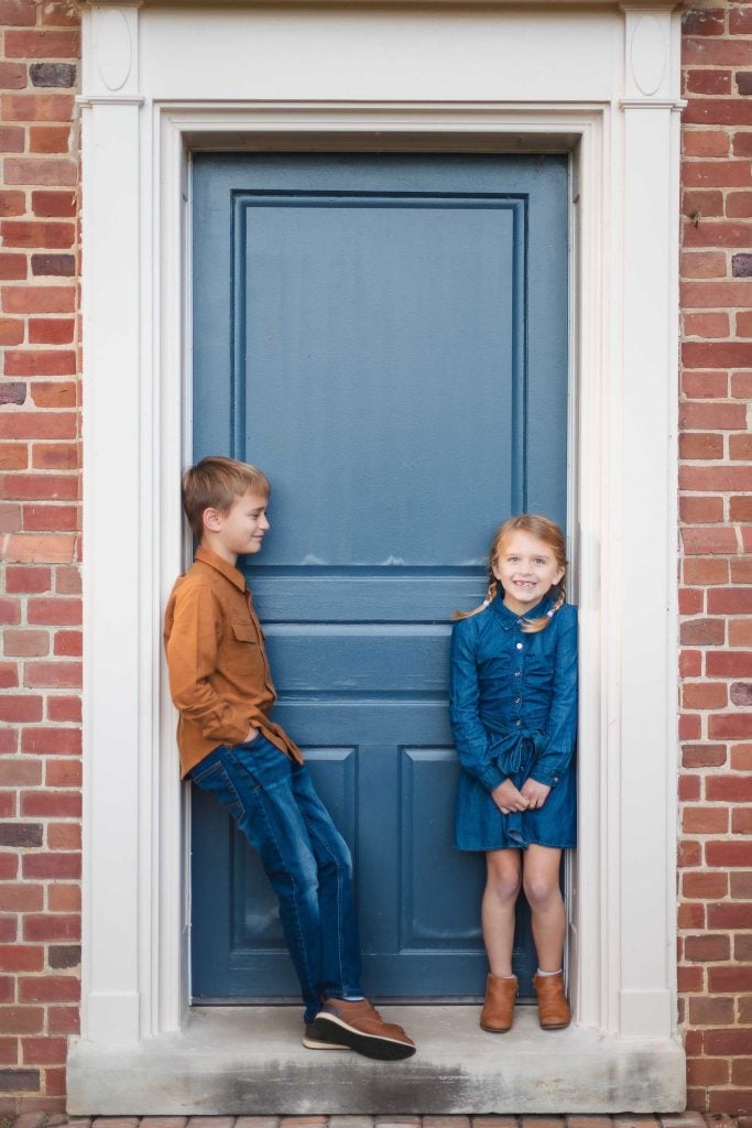 Two children posing for a portrait in front of the blue door at Belair Mansion, with their family.