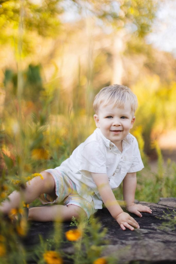 A young boy sitting on a log in Quiet Waters Park, surrounded by a field of wildflowers.