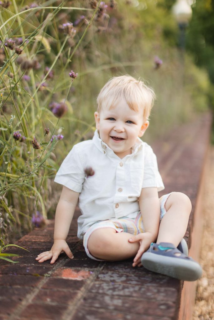 A young boy is sitting on a wooden bench at Quiet Waters Park, surrounded by a vibrant field of flowers.