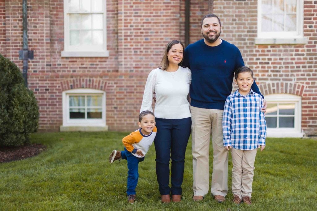 A family of four, including two adults and two children, standing together on a lawn in front of the Belair Mansion in Maryland.