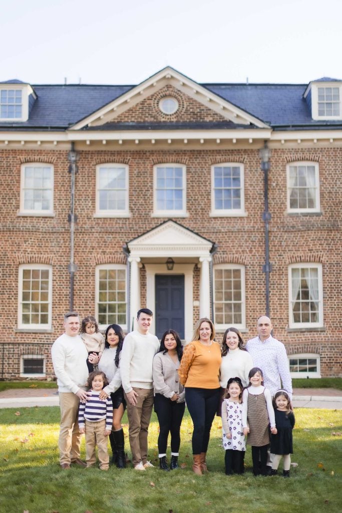 A large family group stands on a lawn in front of the impressive, twostory Belair Mansion, capturing a timeless portrait.