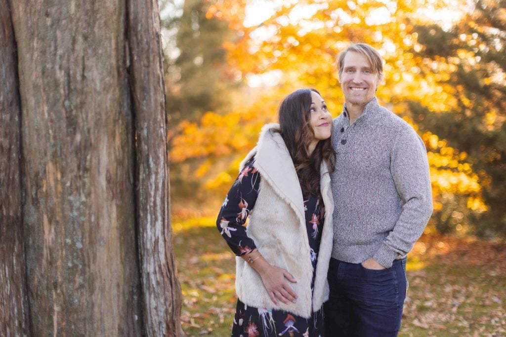 A couple stands beside a tree, the woman looking up at the man, with vivid autumn leaves in the background. In this idyllic outdoor scene near Belair Mansion, their love shines brightly, as if it were a portrait of timeless romance.