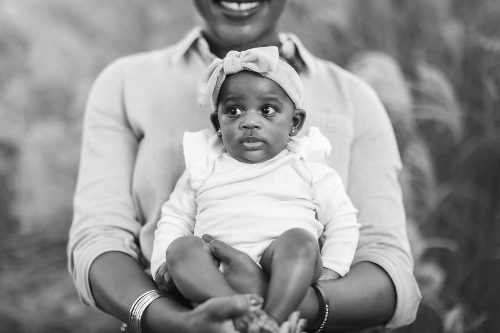 A timeless black and white portrait captures a smiling person holding a baby dressed in a lightcolored outfit with a headband, embodying the essence of family. The person's face is partially visible, adding an intimate touch to the cherished moment.