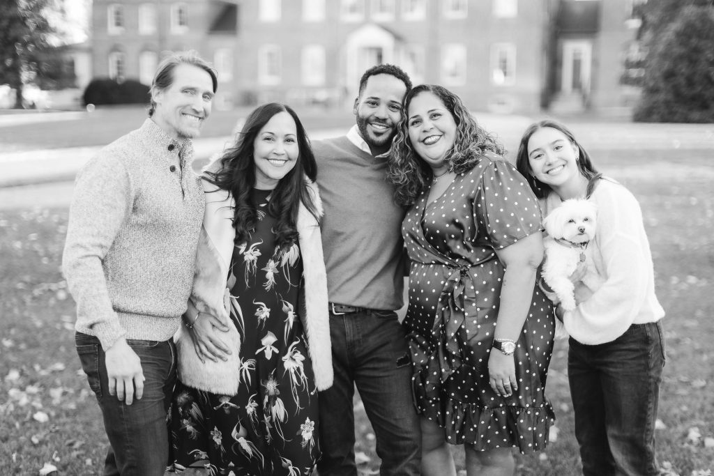 A group of five adults and a small dog pose for a photo outdoors in front of the historic Belair Mansion.