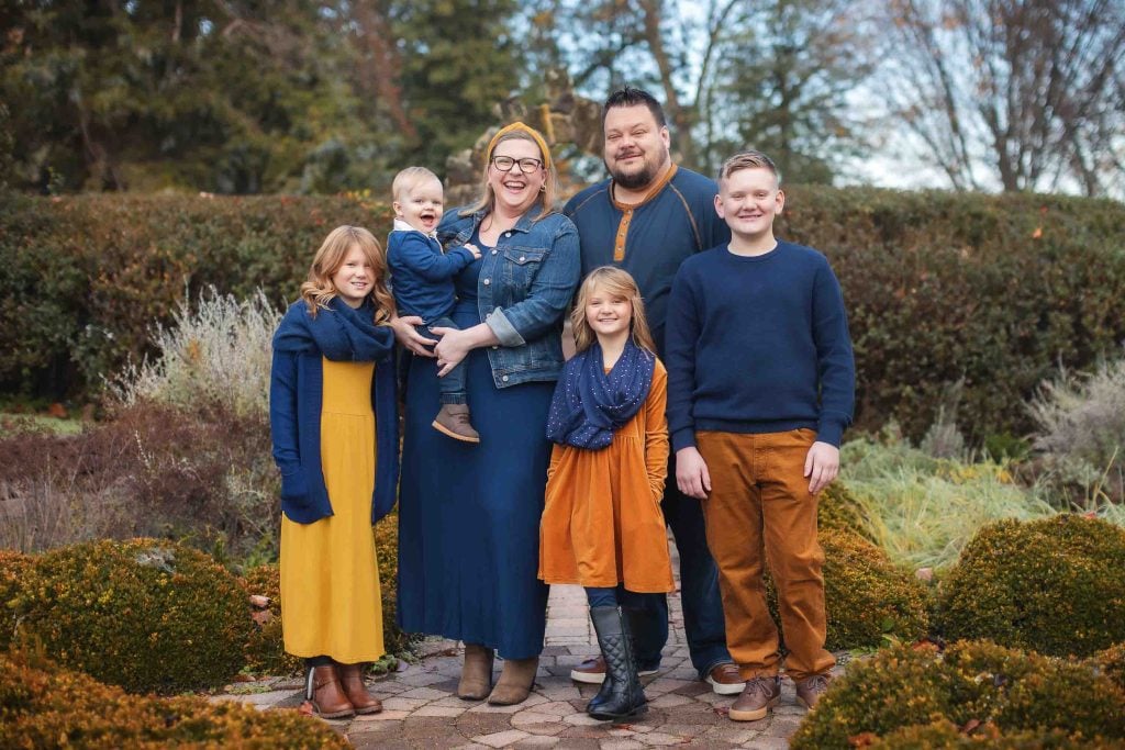 Family Portraits: A family of six posing happily in a garden, with two adults and four children dressed in coordinated autumnal colors.