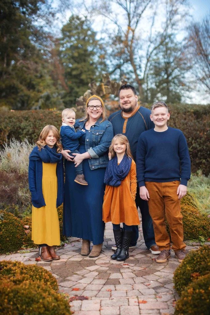 A family of five posing for Family Portraits outdoors, featuring two adults and three children in coordinating autumnal outfits.